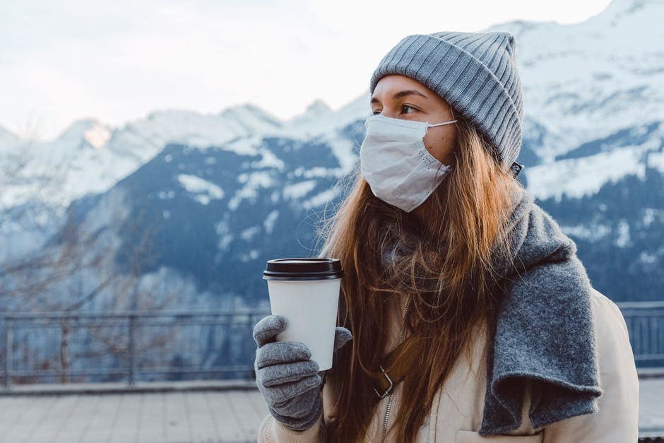 woman in a mask drinks coffee on a background of winter mountains