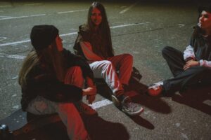 three girls are sitting on the pavement in the evening
