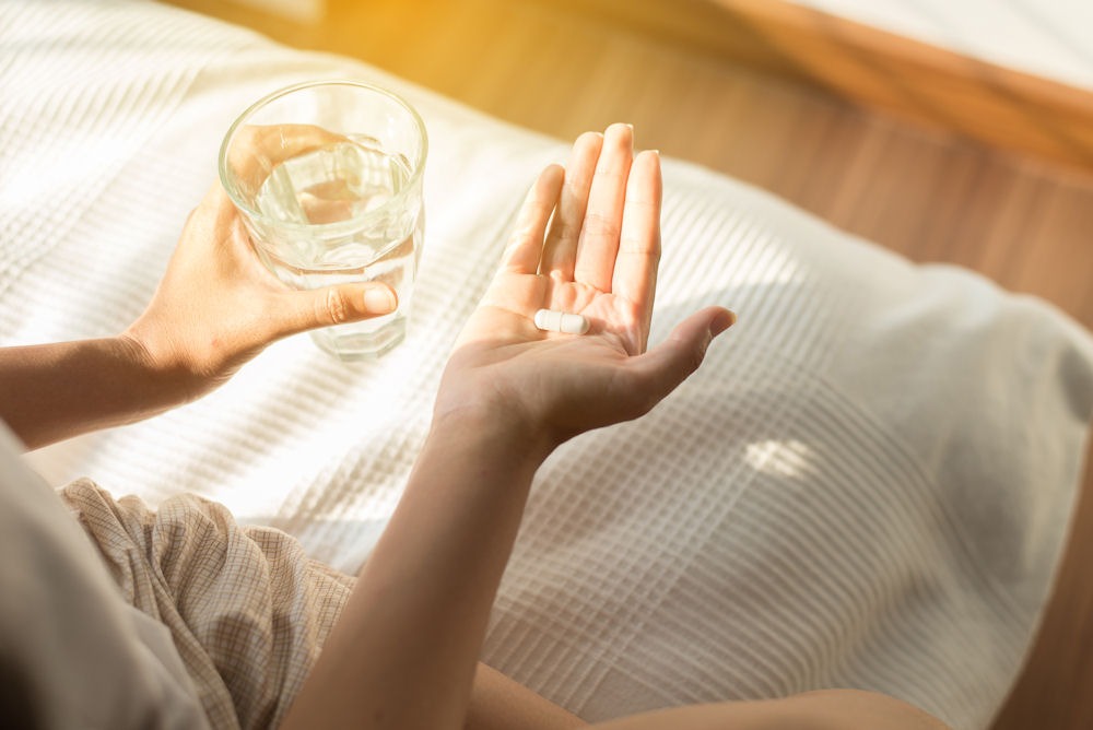 a hand holding a pill while holding a glass of water on the other hand