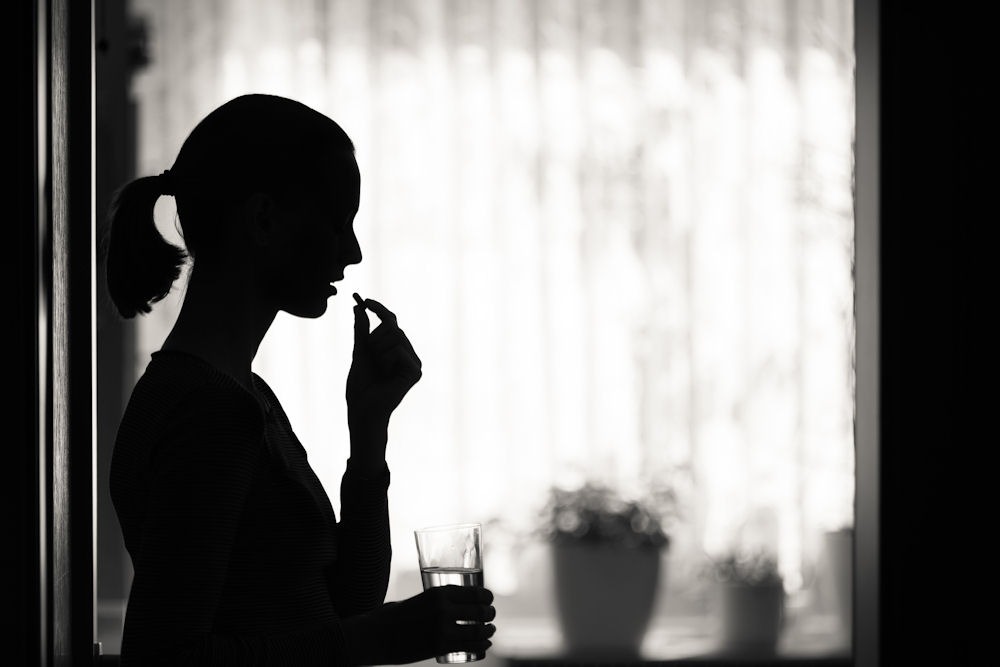 a woman taking a medicine while holding a glass of water