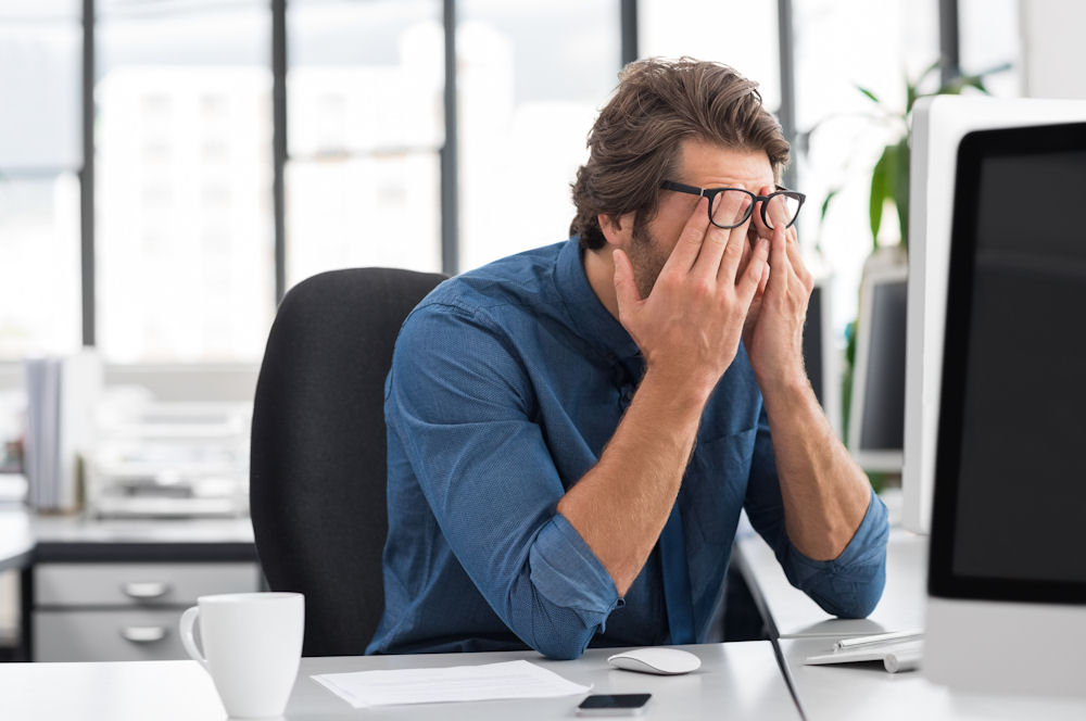 Man at work feeling overwhelmed, showing signs of stress linked to alcohol and cortisol effects.