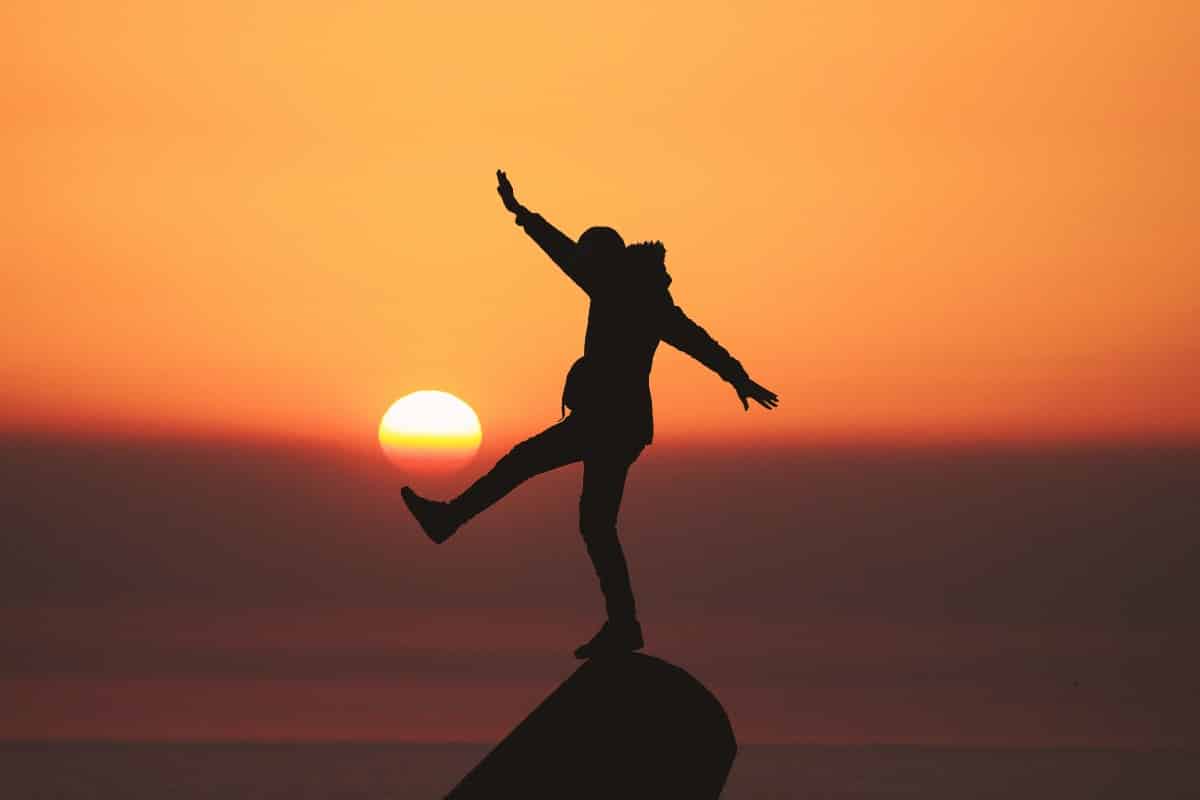 A person balancing on a ledge at sunset, symbolizing the journey to recovery with Ecstasy Addiction Treatment in Orange County.